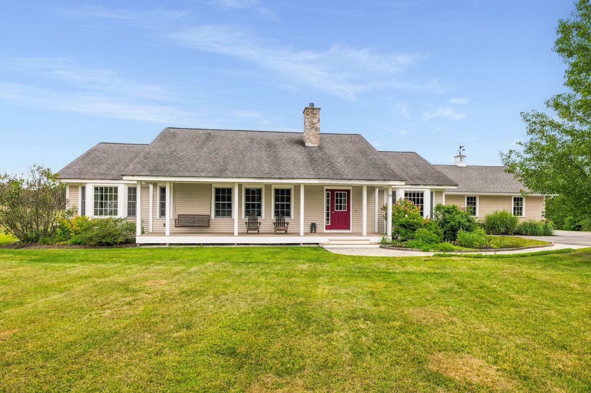 The beige ranch from the front lawn, with the farmer's porch, the red front door, and the garage wing