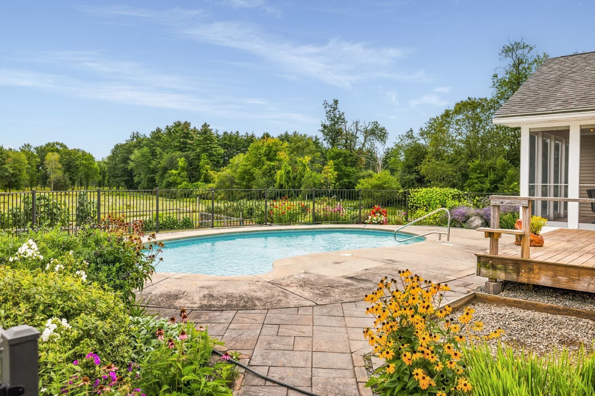 The pool and its fence seen past the flower gardens, with the fields beyond