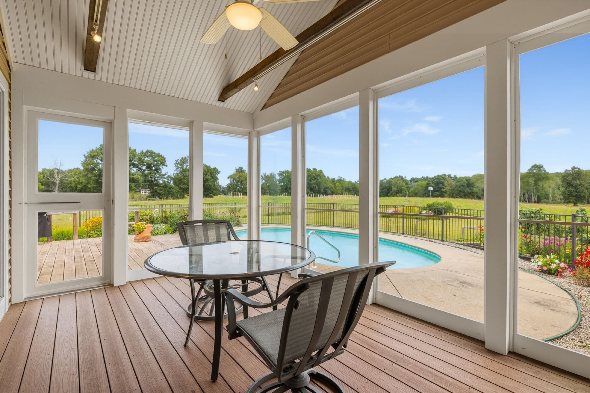 The screened porch with a glass table, looking out over the pool and the fields