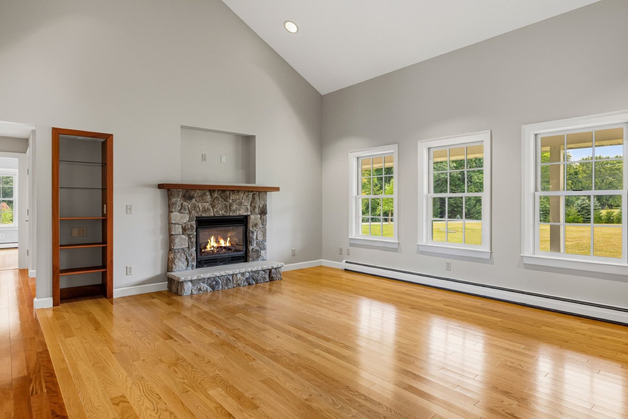 The living room with the stone gas fireplace, a built-in bookcase, and 3 windows